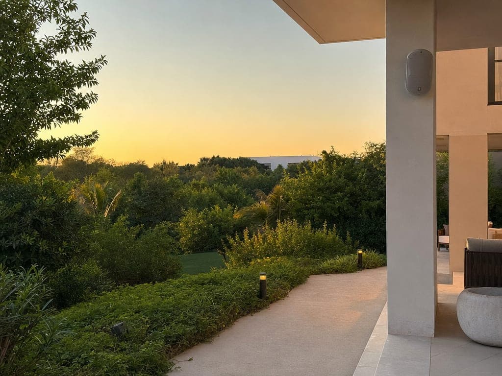 Al Barari villa terrace at golden hour with botanical garden, water feature and warm landscape lighting along the pathway