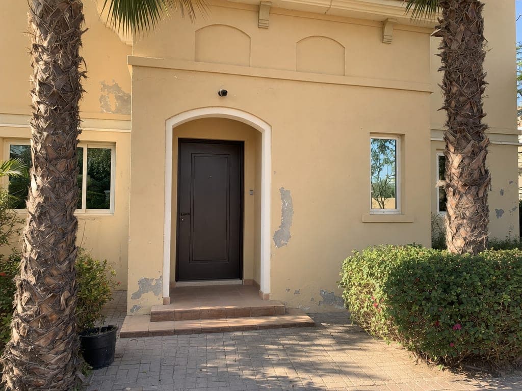 Arabian Ranches villa entrance at golden hour with smart camera and warm interior lighting visible through the doorway