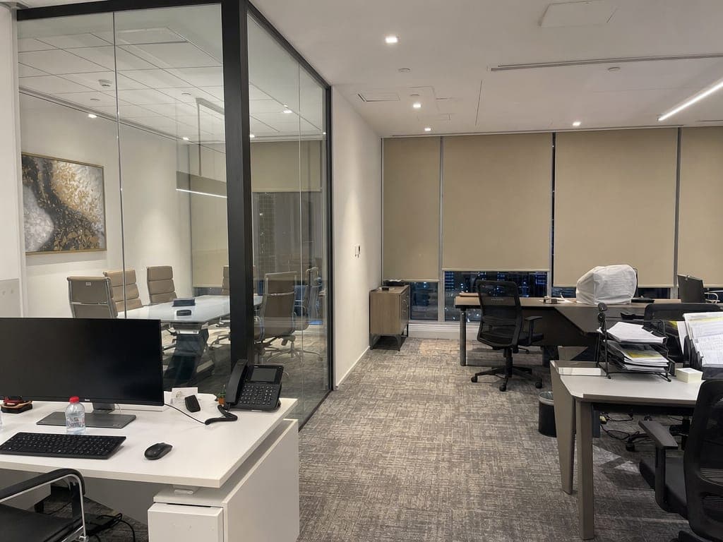 Modern Business Bay office with smart lighting, automated blinds and conference room visible behind, evening canal view through windows