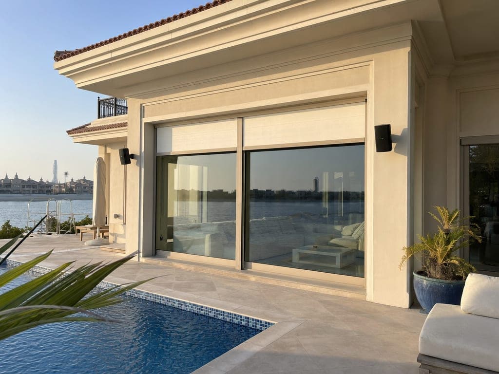Palm Jumeirah frond villa pool deck at golden hour with smart blinds raising on the living room glass behind
