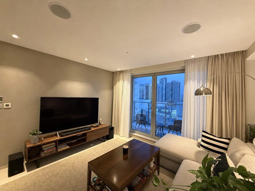 Sharjah apartment living room with in-ceiling Sonos speakers, kitchen and dining visible behind, warm evening scene lighting