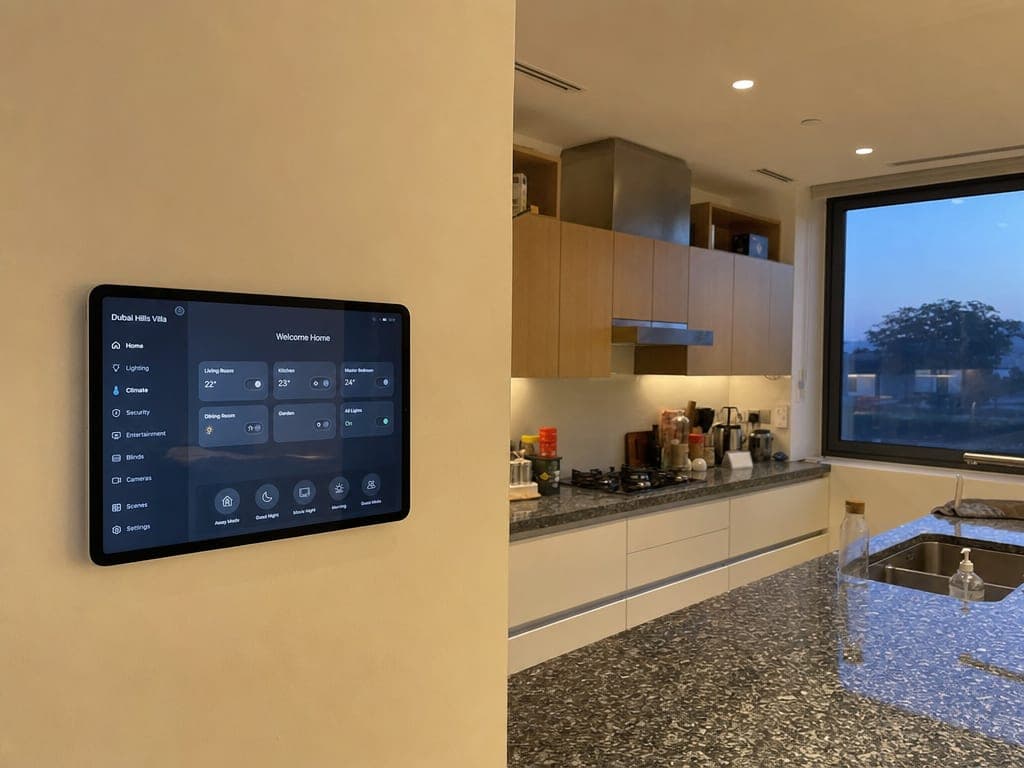 Open-plan Dubai Hills villa kitchen with a wall-mounted smart home tablet and warm scene lighting