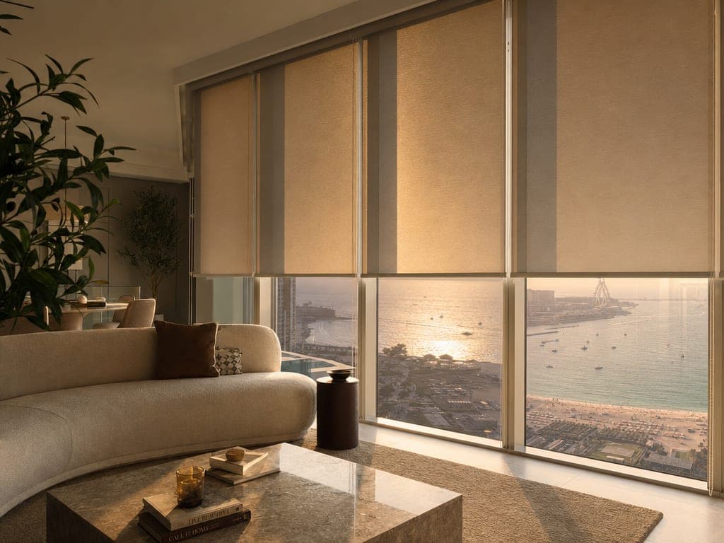 Motorized blinds half-closed in a sun-facing JBR apartment with afternoon light filtered to a warm glow