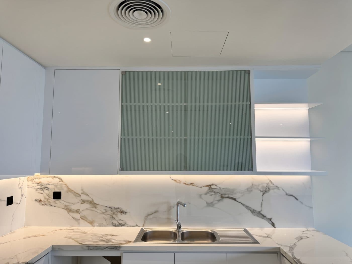 Kitchen in a California Village townhouse with warm LED strip lighting under the wall cabinets and on the open shelves